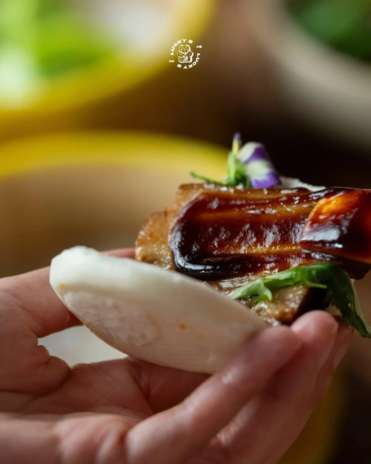 A soft steamed bao bun filled with glazed pork, held in hand